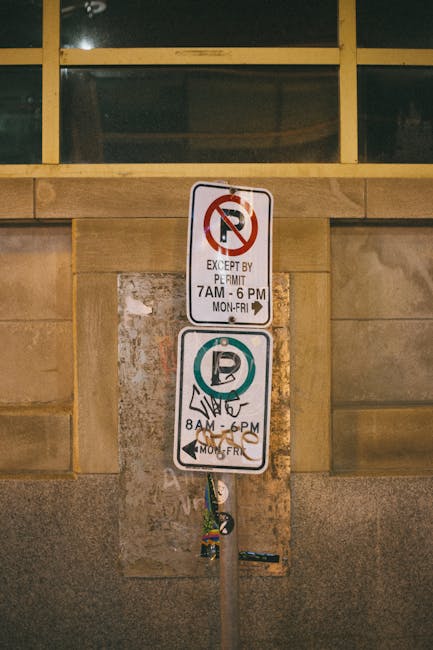 The image shows two parking restriction signs mounted on a beige brick wall, with the top sign indicating no parking except for permit holders between 7 am and 6 pm from Monday to Friday, and the bott