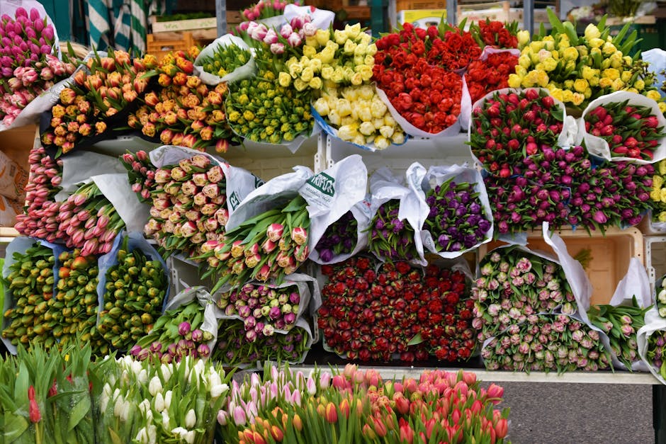A vibrant display of fresh flower bouquets arranged on display shelves at a flower shop, featuring a variety of tulips, roses, and mixed floral bunches in shades of pink, red, yellow, purple, and whit